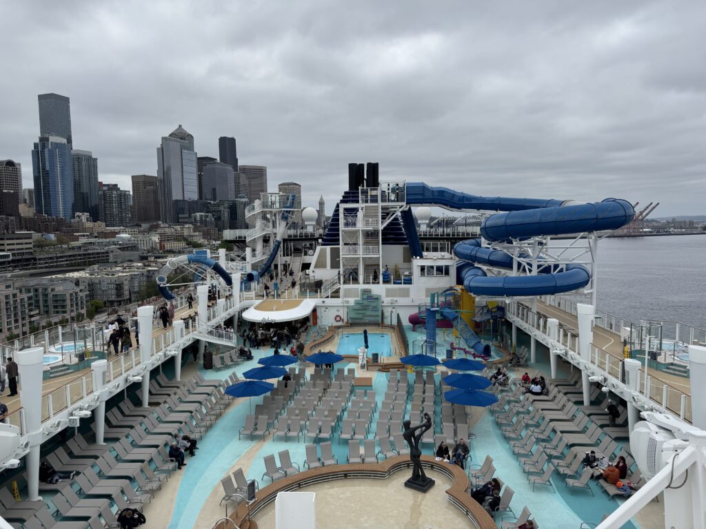 The waterslides and pool deck of Norwegian Encore with the Seattle skyline behind
